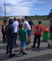 Dwie policjantki stoją przy skateparku na terenie Ośrodka Sportu i rozmawiają z grupą 8 chłopców w wieku 12-15 lat.