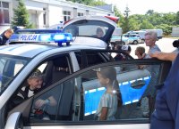 policjant stoi przy radiowozie z prawej strony, na siedzeniu kierowcy siedzi chłopiec.