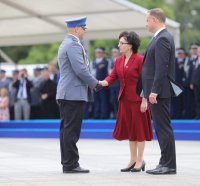 PO lewej stronie stoi policjant w mundurze galowym, po prawej stronie stoi Prezydent Andrzej Duda oraz Minister Spraw Wewnętrznych i Administracji, która podaje uścisk dłoni policjantowi.
