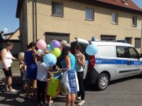 dzieci z opiekunami stoją przy radiowozie oznakowanym, policjanci rozdają balony dla najmłodszych.