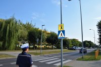 Policjantka ruchu drogowego stoi przy przejściu dla pieszych oznakowanym pionowo i poziomo tuż przy szkole.