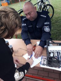policjant siedzi przy stoliku, kobieta podpisuje dokument wypelniony przez policjanta dotyczący znakowania roweru