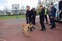 Przy radiowozie policji stoją uczniowie klasy policyjnej, policjant i pies służbowy.